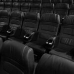 Black and white image of empty leather seats in an indoor movie theater.