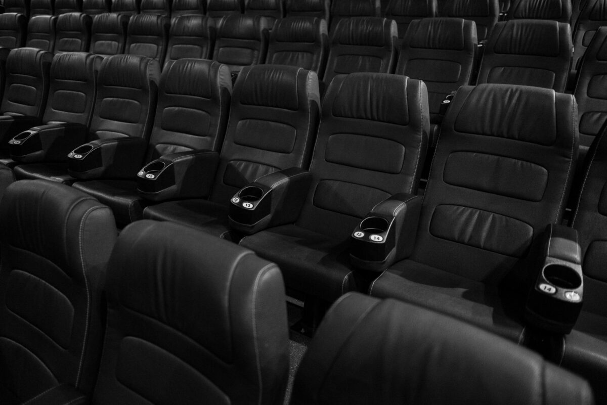 Black and white image of empty leather seats in an indoor movie theater.